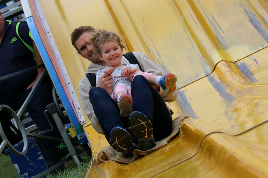 A man and little girl ride a slide.