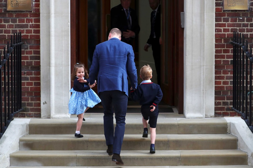 Prince William, Prince George and Princess Charlotte walk upstairs into a hospital with Princess Charlotte waving.