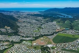 Aerial view of Cairns shows township, blue sky, mountains, sea in the distance.