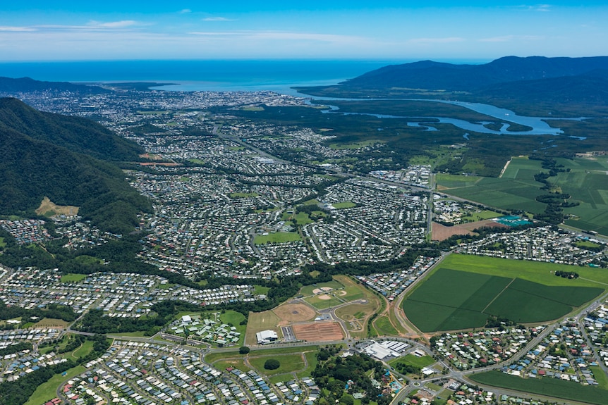 Aerial view of Cairns shows township, blue sky, mountains, sea in the distance.