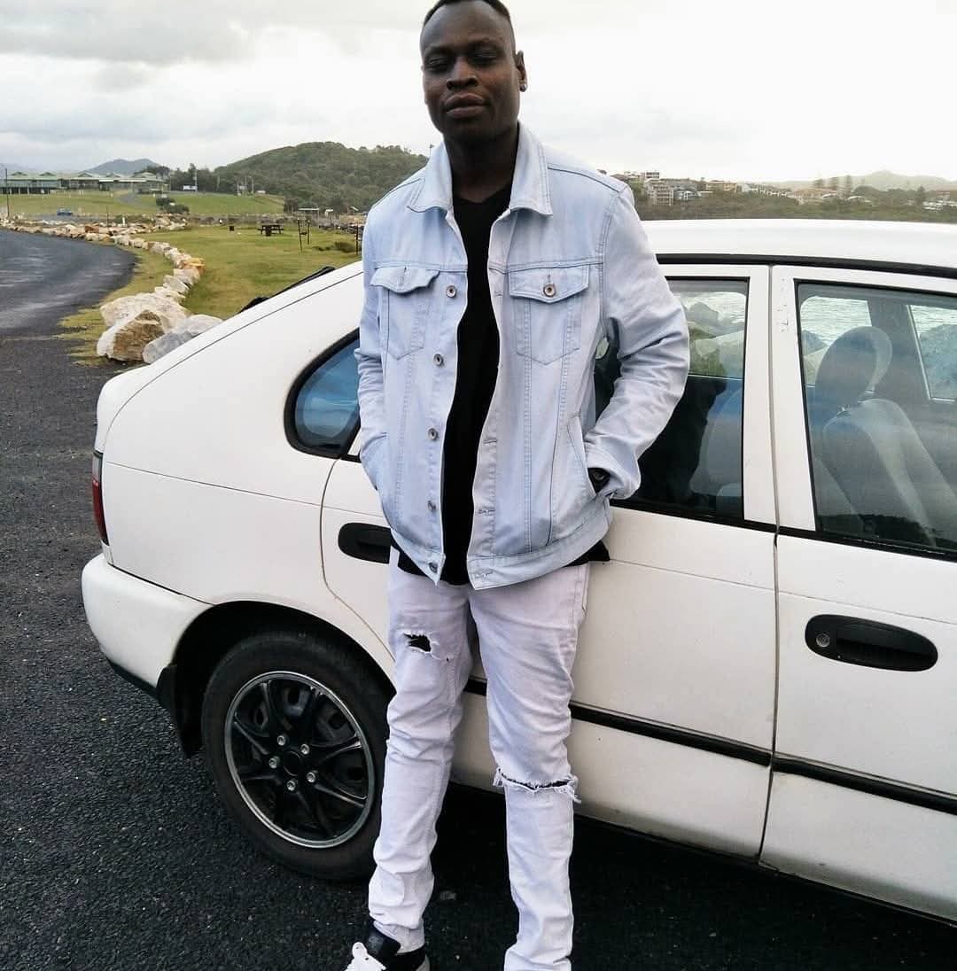 Young African Australian man stands in front of car on headland
