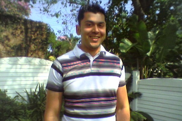 A young man in a striped polo shirt photographed in a garden.