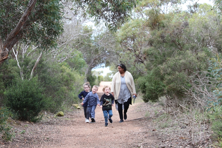 Indigenous woman walking along bush trail with three little children.