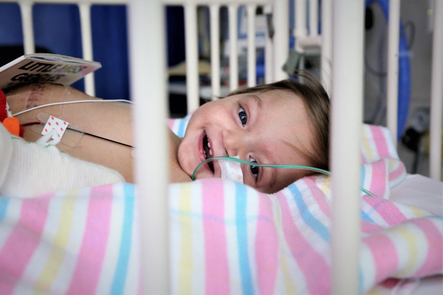 A baby in a hospital cot smiling through the bars.