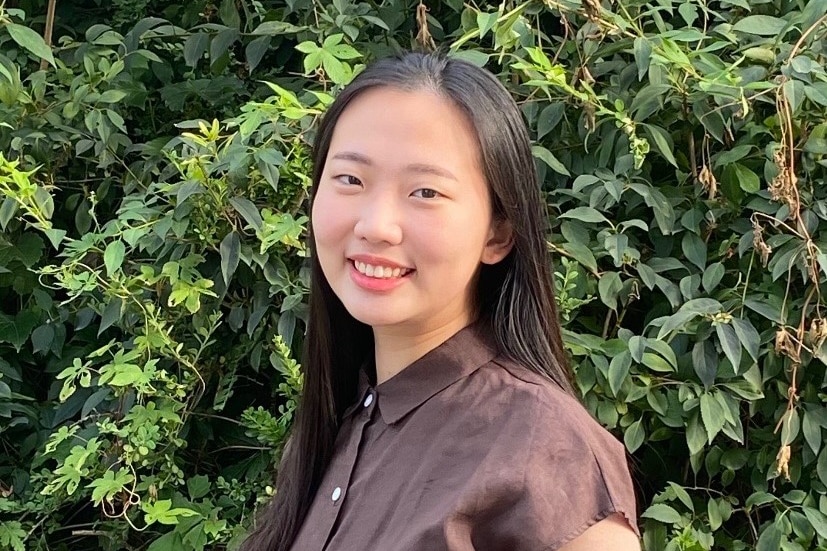 Katrina smiles for a photo in front of a green hedge.