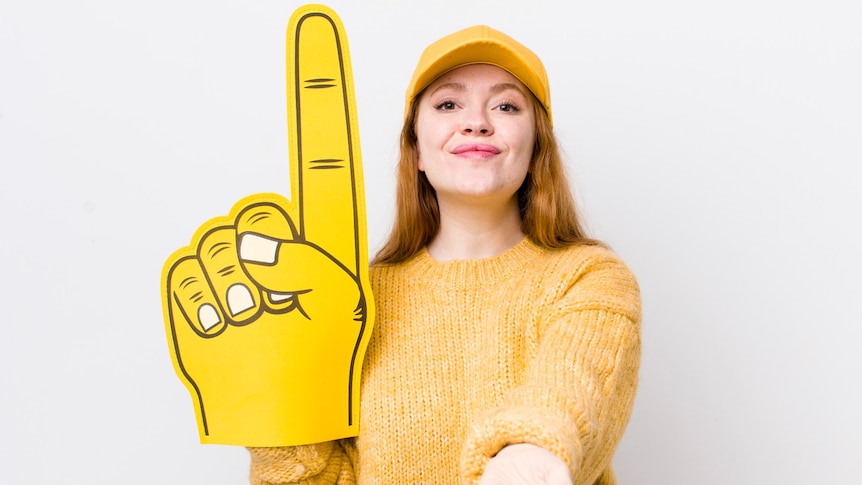 A smiling woman holding an oversized hand with one finger up