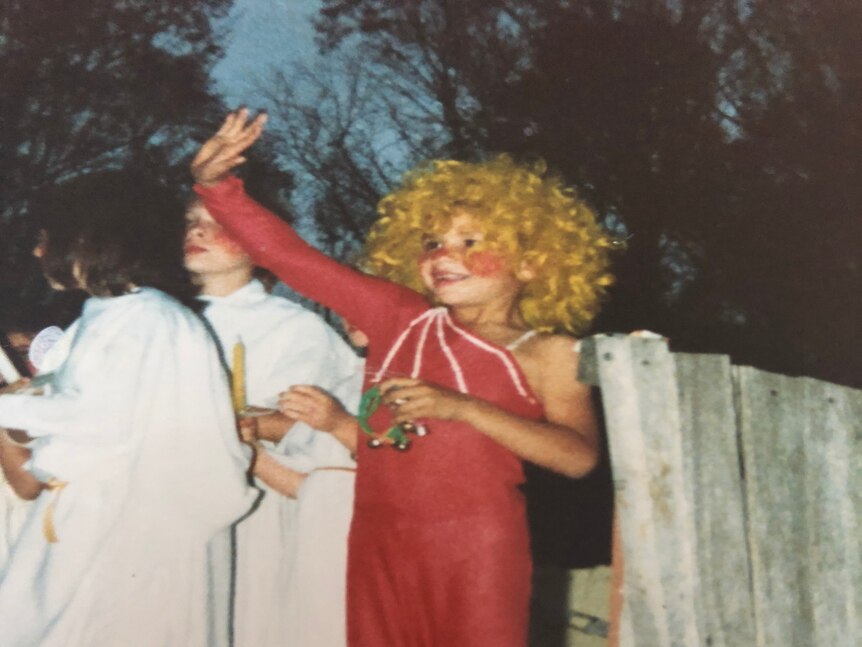Daniel as a child wearing a blonde curly wig and red dress