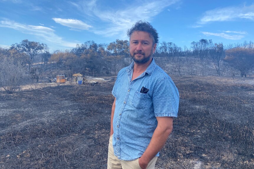 Man in blue shirt with black back ground, burnt ground and trees