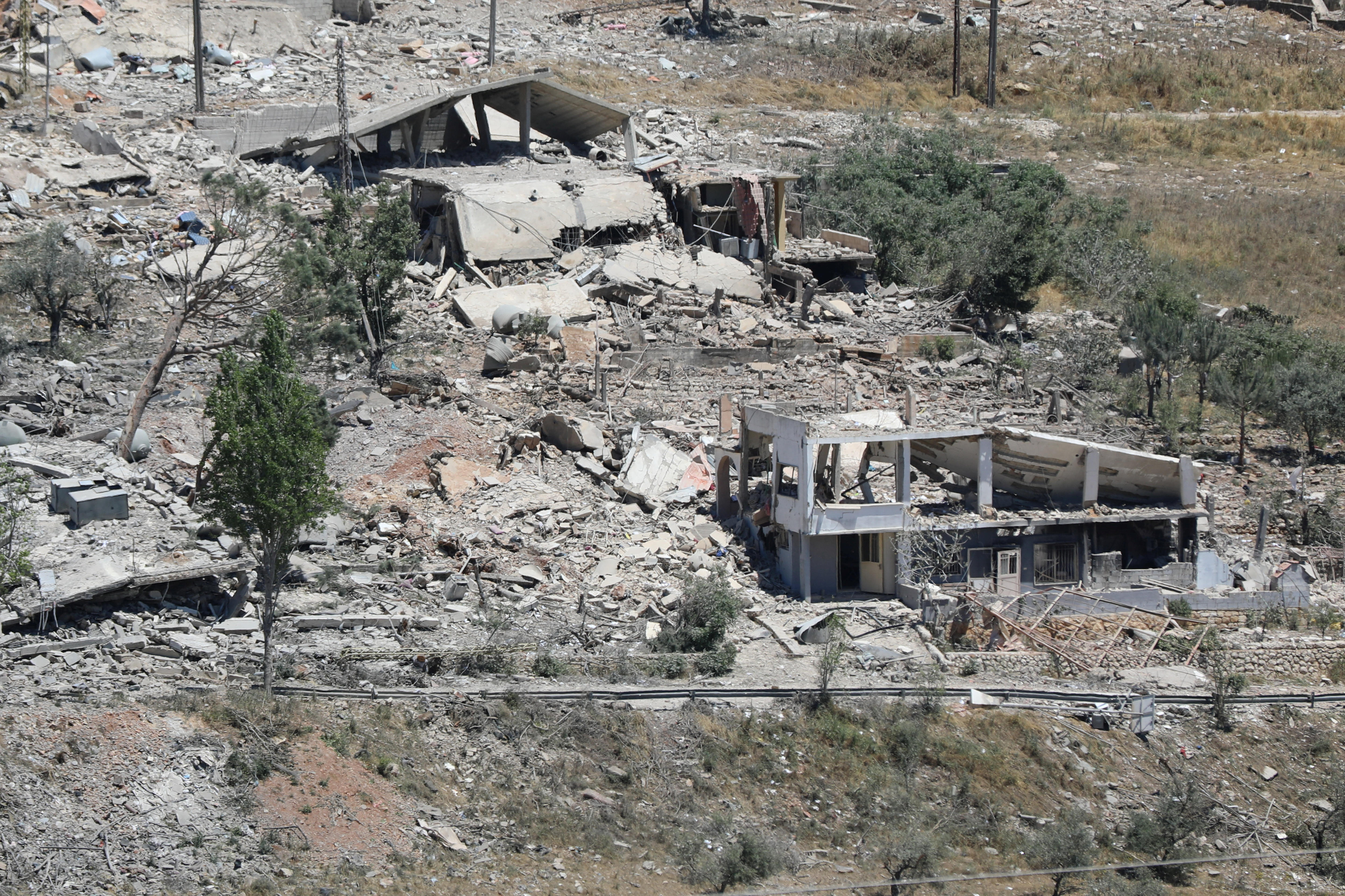 A destroyed building with grey rubble and dirt around a patch of land 