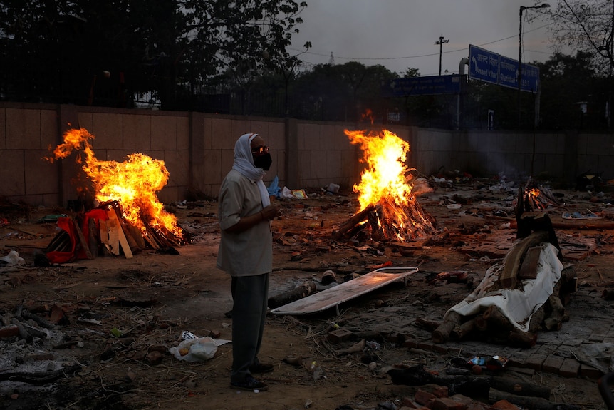 A man in a gas mask stands next to a funeral pyre.