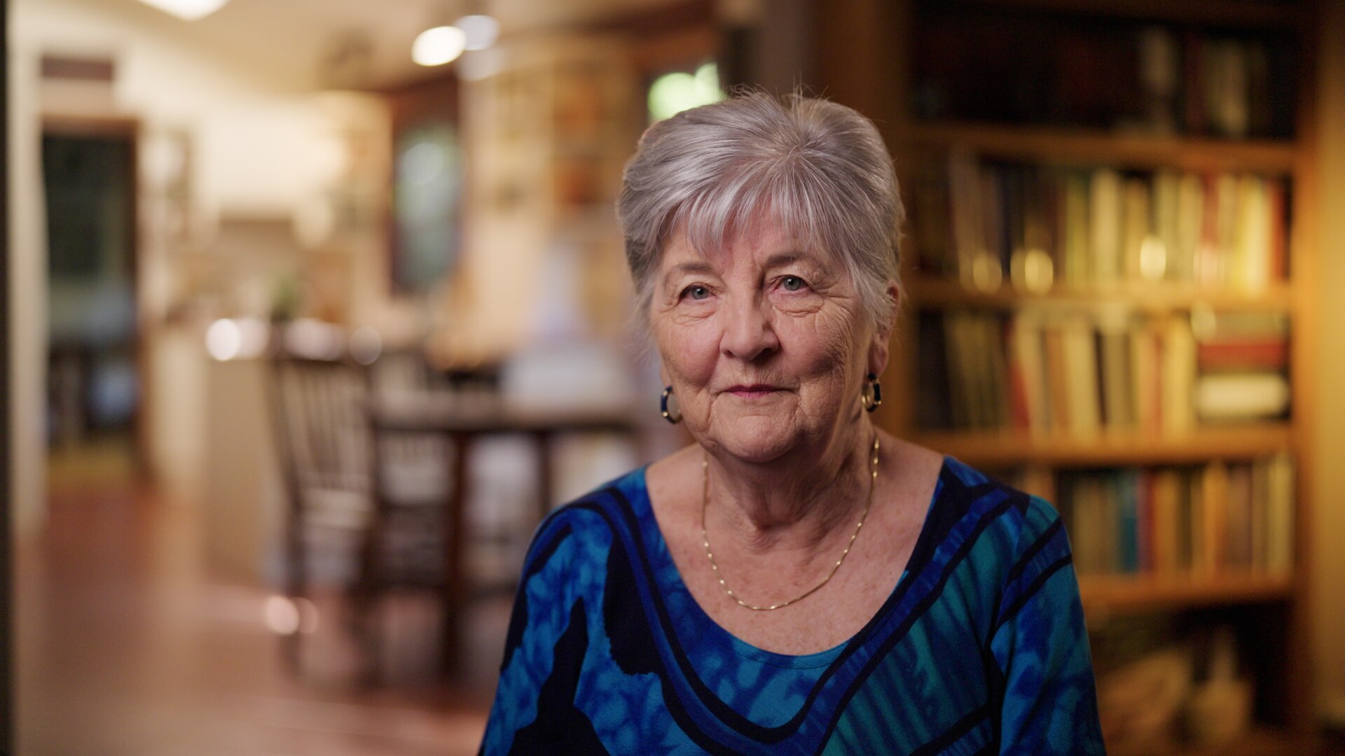 Grey haired woman sits in living room with bookshelves behind her