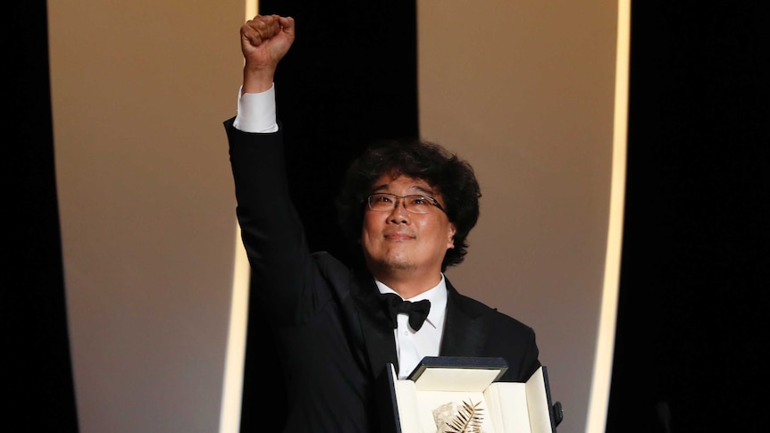 A Korean man holds a black leather box containing a metal palm as he throws is fist in the air onstage.