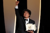 A Korean man holds a black leather box containing a metal palm as he throws is fist in the air onstage.