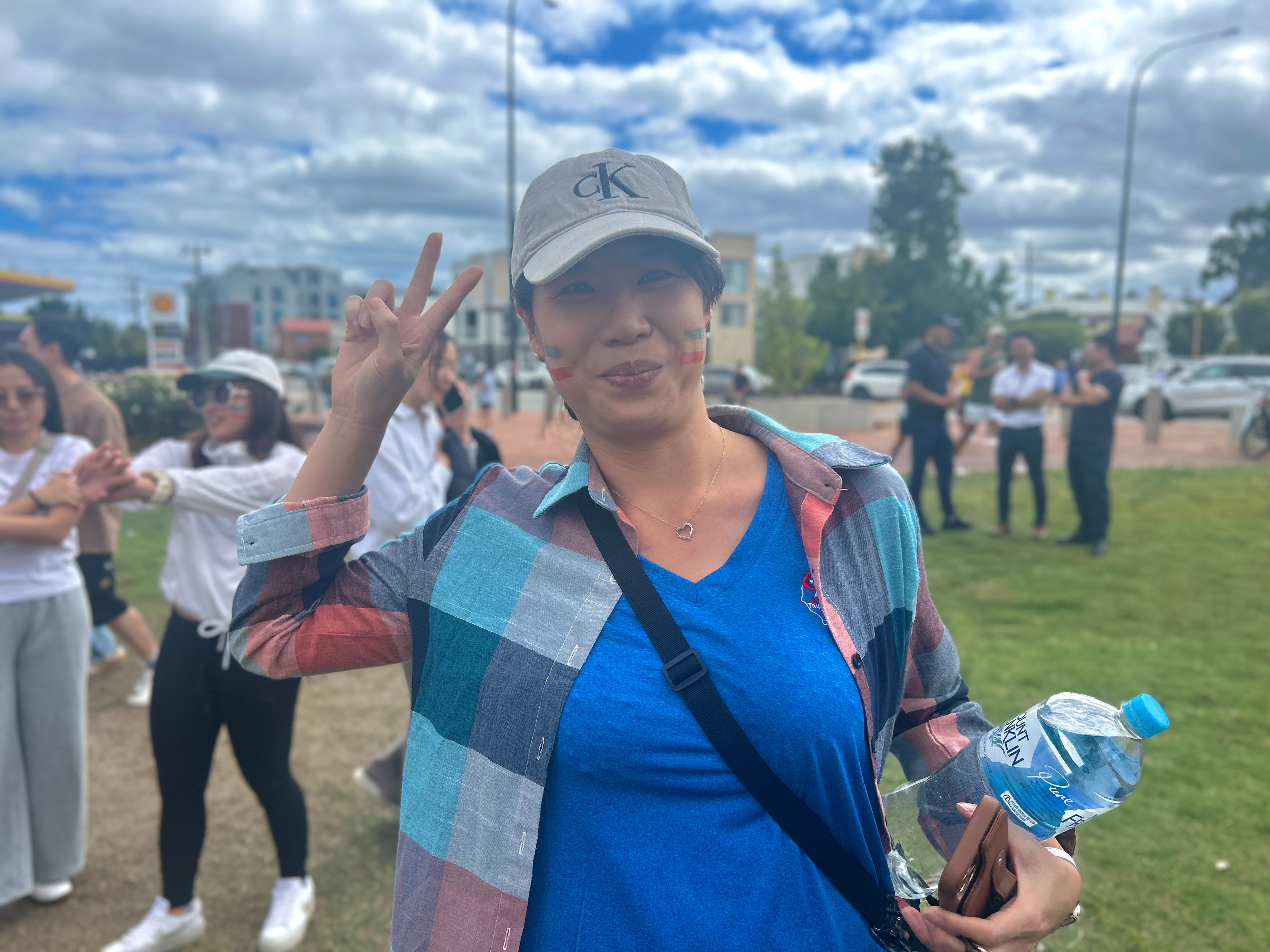 Uma mulher de camisa azul sorri e faz o sinal da paz com a mão