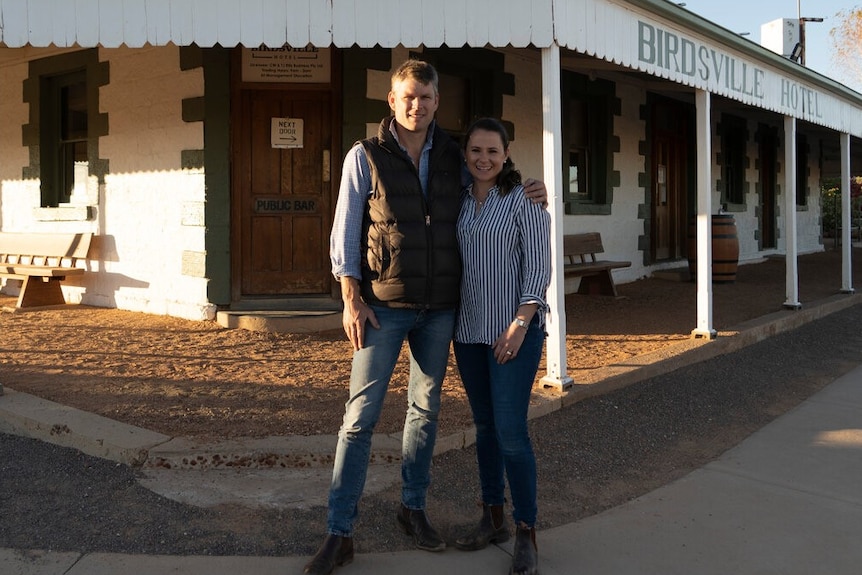 A man and woman with their arms around each other in front of the Birdsville Hotel.