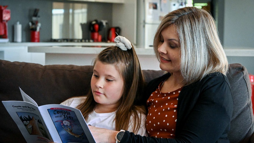 Kylie Mackie reads a book with her daughter Jorja on the couch in their home.