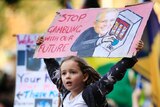 A young girl holds a sign that says "stop gambling with our future" during a climate change rally.