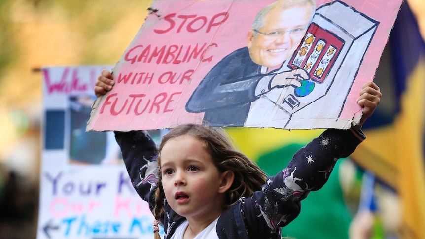 A young girl holds a sign that says "stop gambling with our future" during a climate change rally.