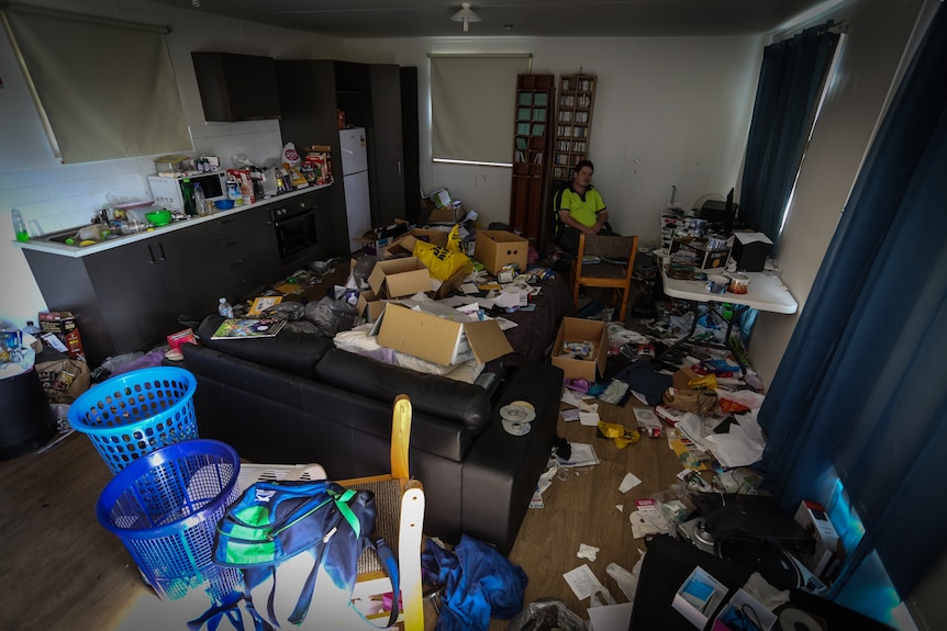 Warwick Allen in his very messy loungeroom filled with rubbish from one end to the other.