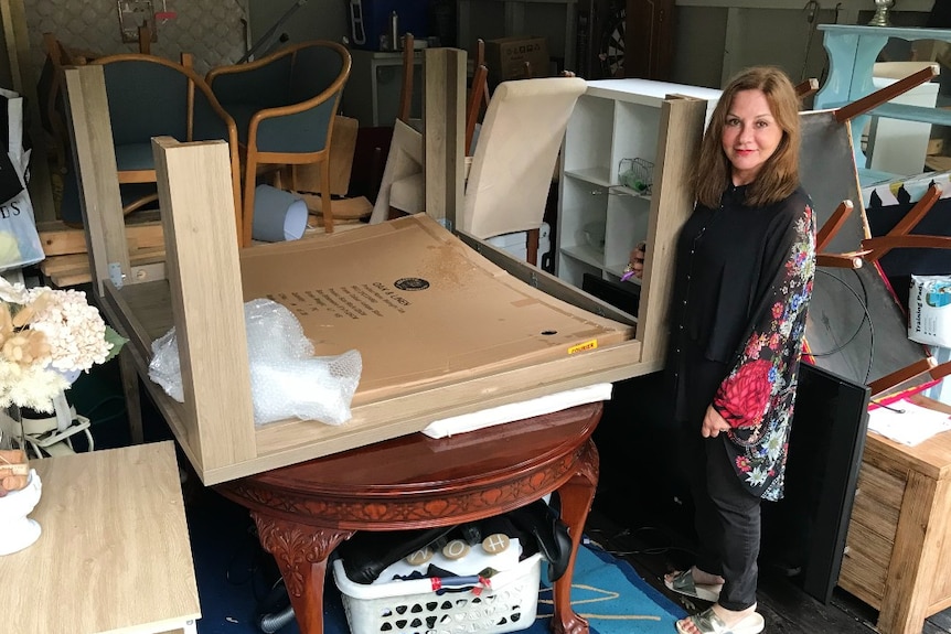 A woman stands in front of a garage full of furniture