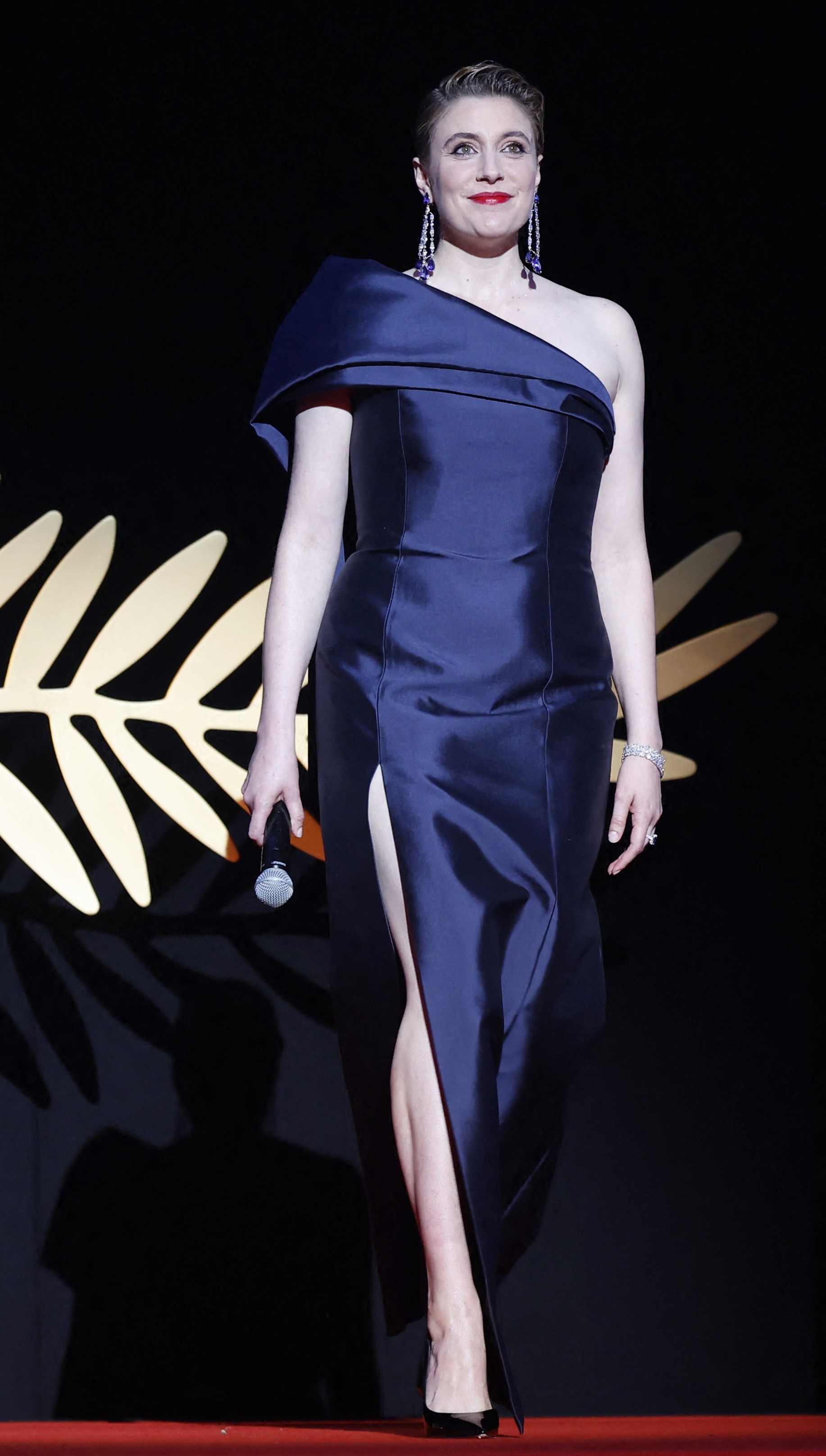 Greta Gerwig wearing a dark navy blue off-the-shoulder dress with an oversized sleeve and a high slit
