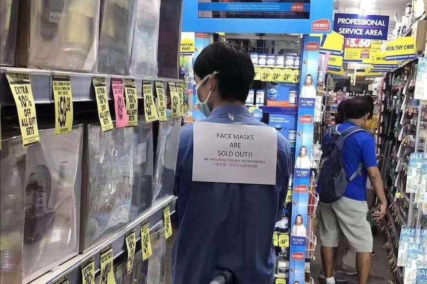 A staff member wears a sign saying 'face masks are sold out'