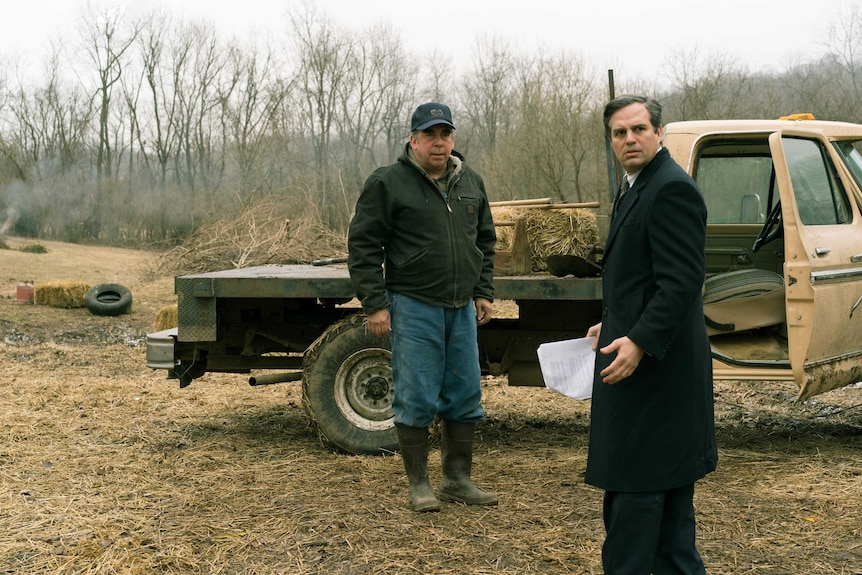 The actors Bill Camp as a farmer and Mark Ruffalo as a lawyer standing in a dry farm field with a pickup truck