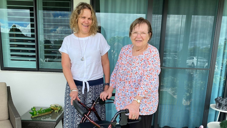 Two women smiling at the camera holding onto a walking aid. 