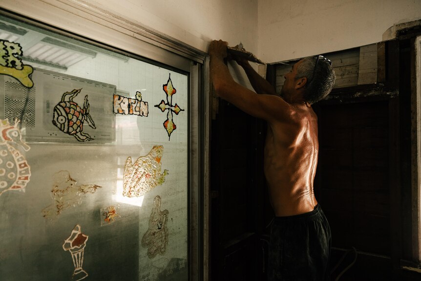 A shirtless man strips the walls of a flood-ravaged home