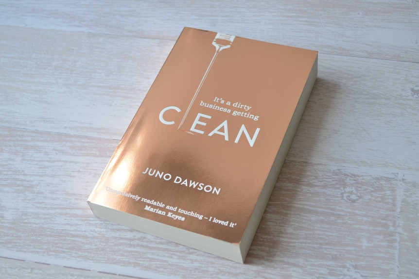 A book with a shiney gold cover, Clean by Juno Dawson, on a light wooden table.