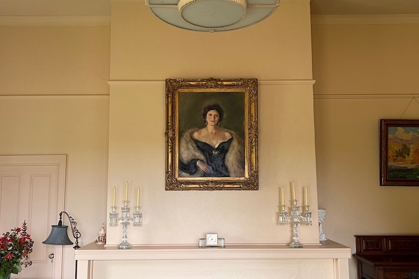 A portrait of a beautiful woman in a black dress hangs on a wall above a fireplace