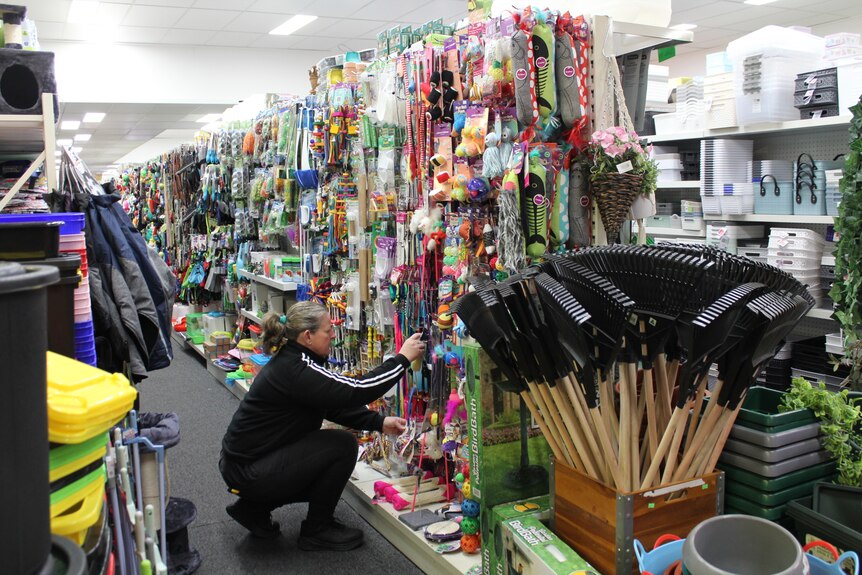 A woman in a black tracksuit crouching down, rearranging stock at a retail store.