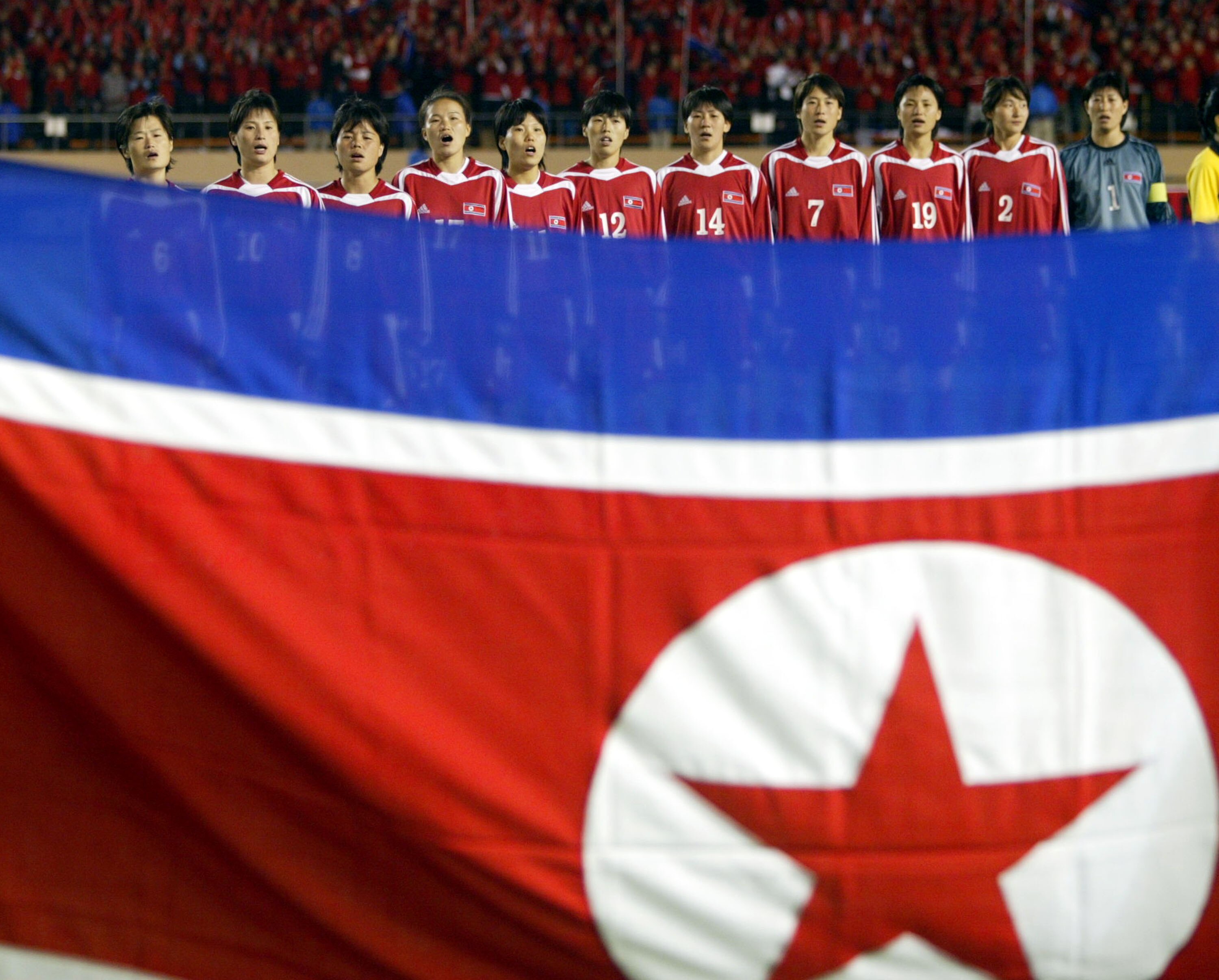 A soccer team wearing red and white stands behind a flag of red, white and blue in a line