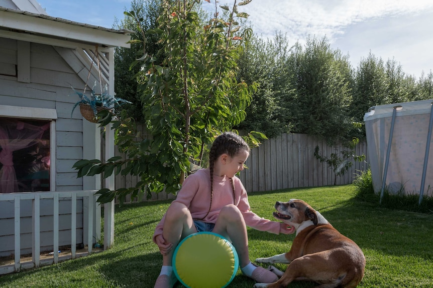 A little girl in a pink sweater plays with a dog in her backyard