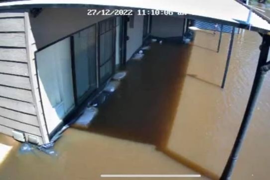 Security camera footage of a white weatherboard shack, it is around half a metre under brown flood waters