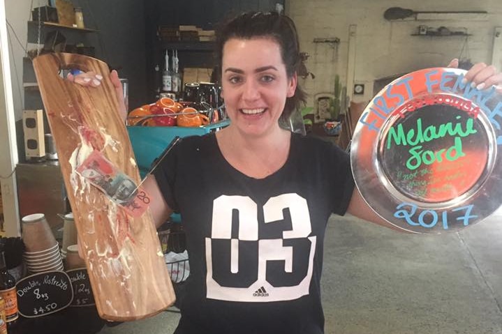 woman stands with empty chopping board, plate with her name on it and is smiling.