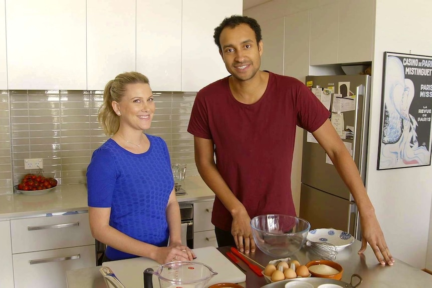 Man and woman in their thirties stand around cooking ingredients in the kitchen.