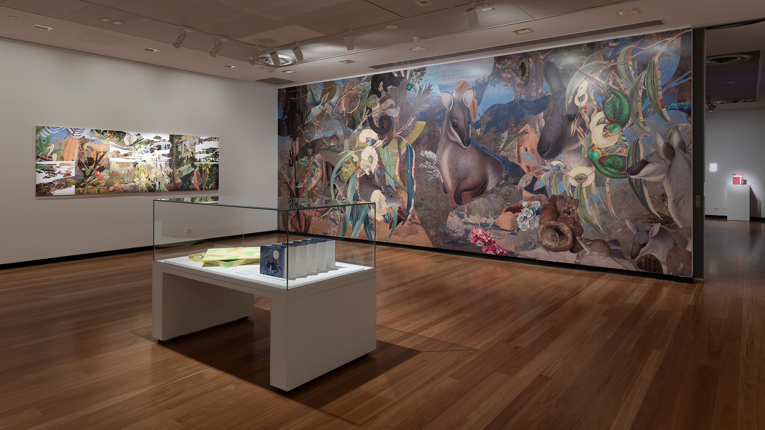 An artwork depicting Australian native flora and fauna on the wall of a gallery; a glass cabinet in the middle of the room.