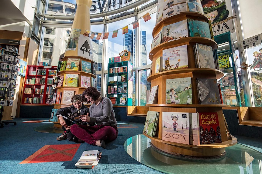 Colour photograph of mother and son reading a book in the children's books section in a Books Kinokuniya.