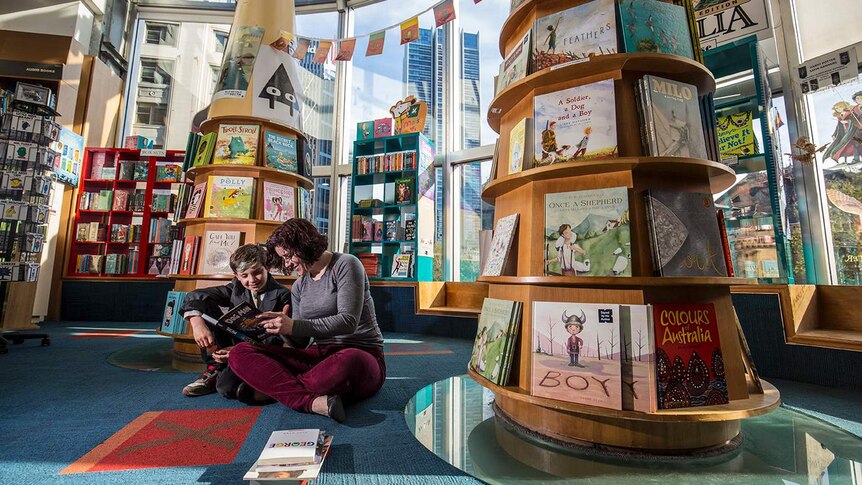 Colour photograph of mother and son reading a book in the children's books section in a Books Kinokuniya.
