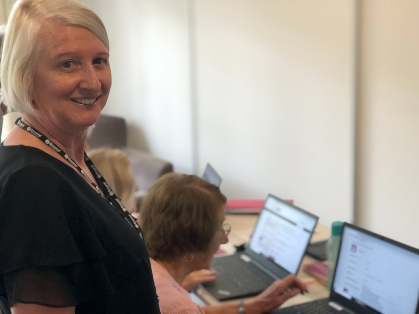 Woman standing behind seniors who are looking at laptops.