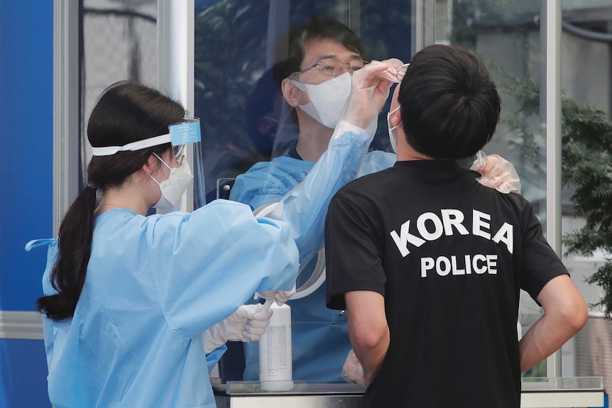 Two medical workers take samples from a police officer during COVID-19 testing in South Korea