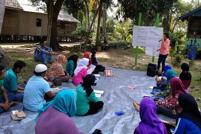 A woman standing next to a chart in front of a group of people sitting on the ground.