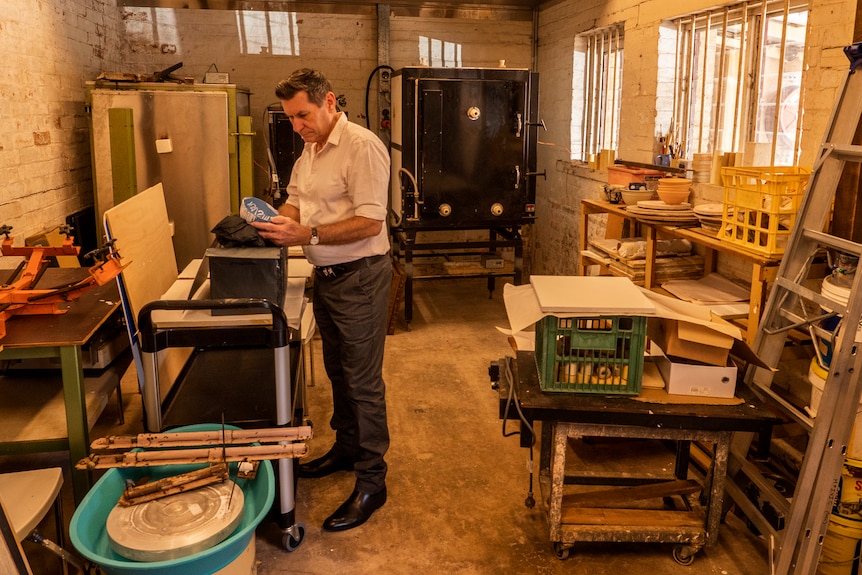 A man stands in a clay work shop space with kilns in the background.