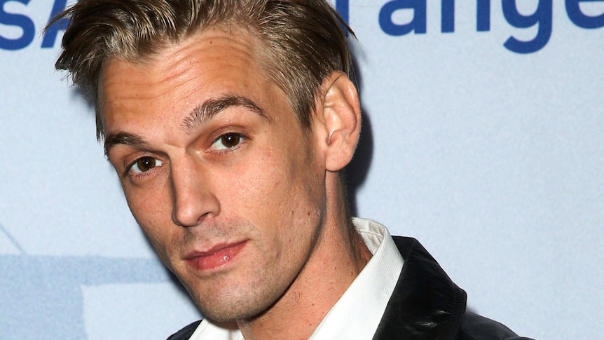 a close up image of Aaron Carter raising his eyebrows as he looks at the camera on a red carpet event