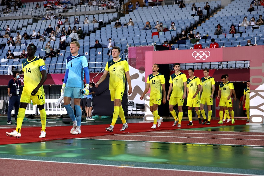 A men's soccer team wearing yellow and green walks out of a tunnel before a match