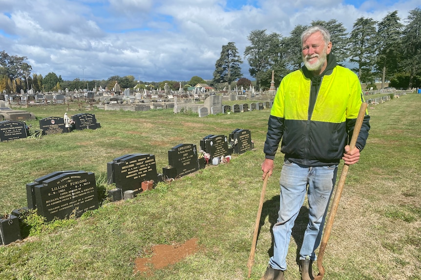 man standing in a graveyard with a pick and shovel. 