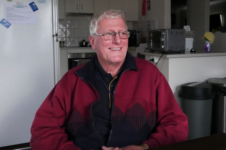 man in a red jacket sitting at a kitchen table