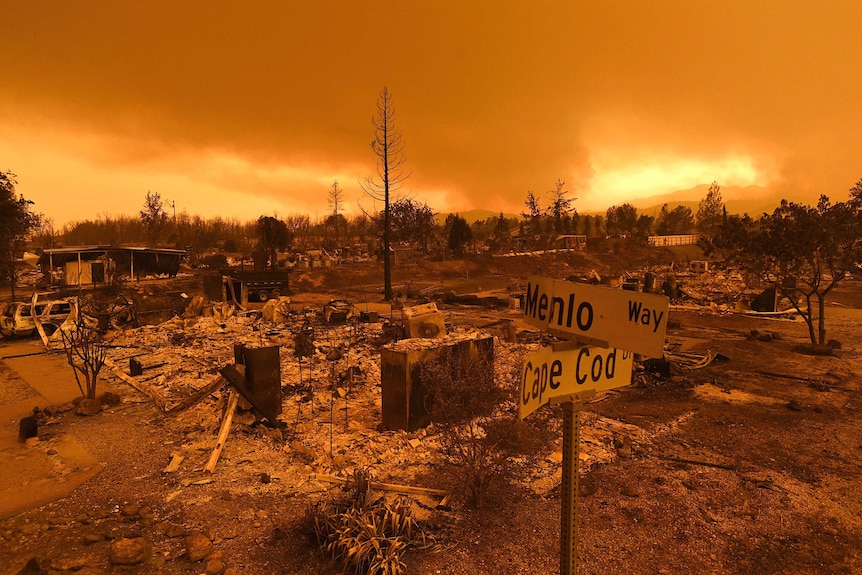 The sky glows orange above burnt out homes