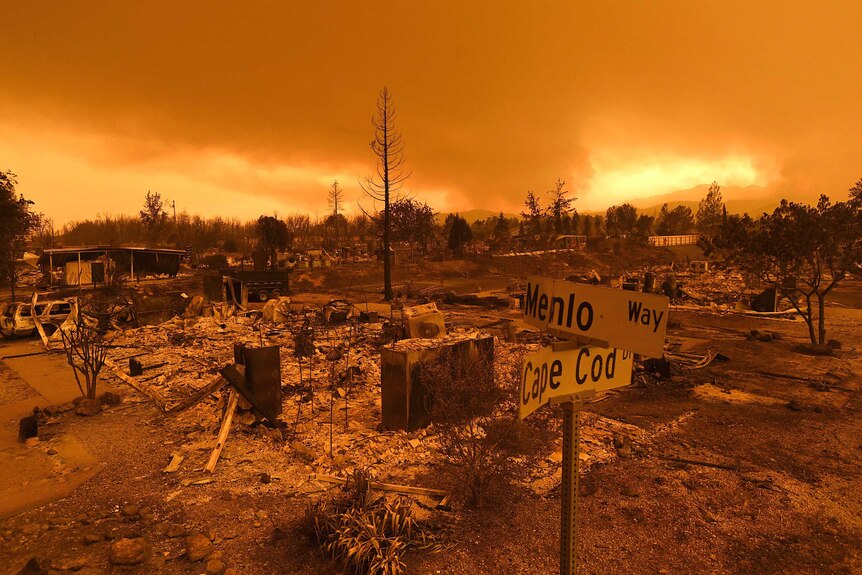The sky glows orange above burnt out homes